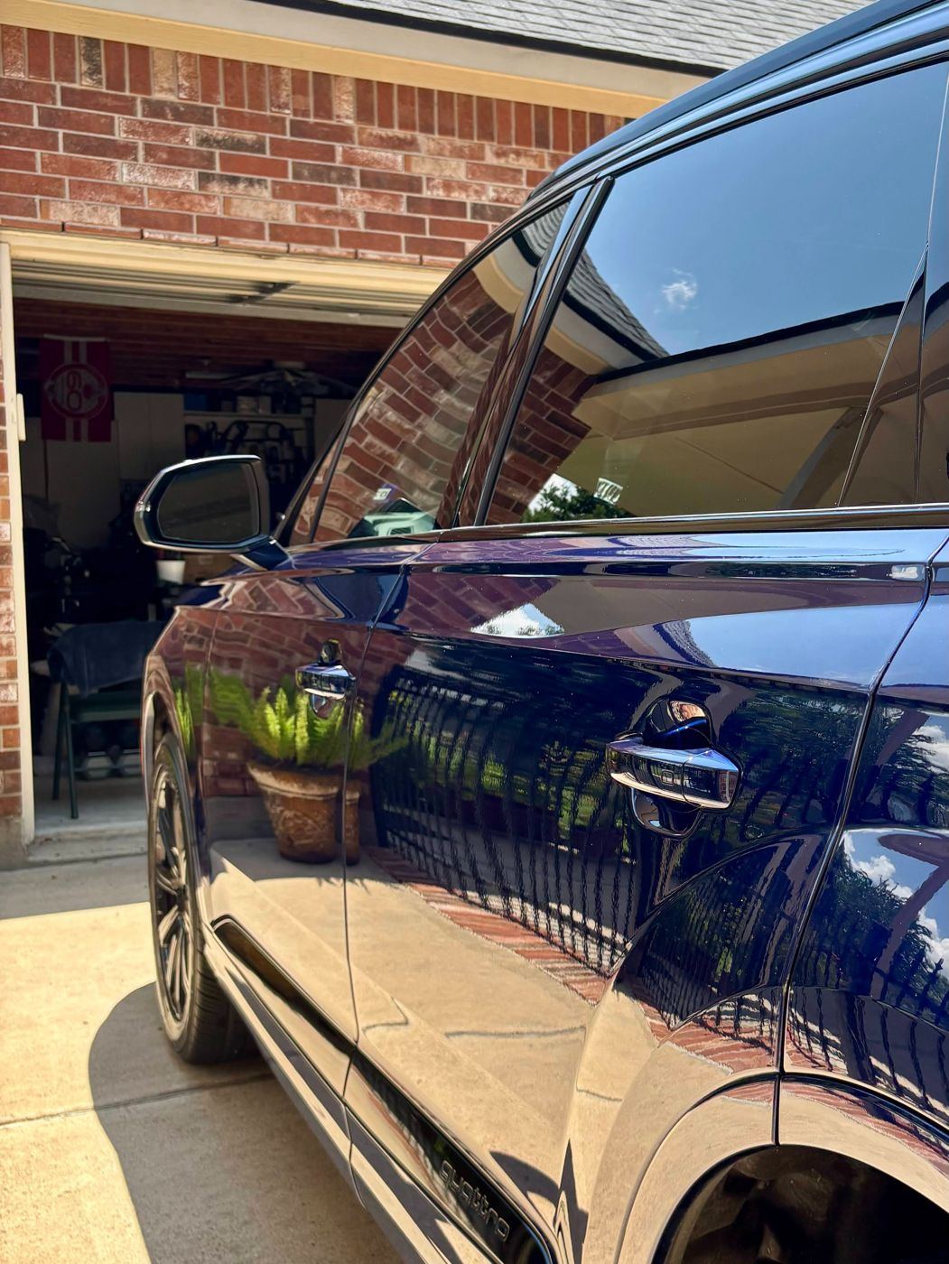 Mirror-like reflections of brick and plants in the door of a blue Audi Q7