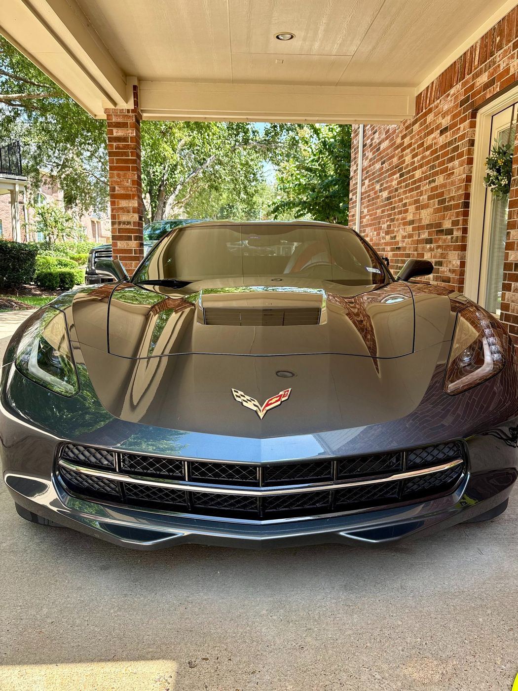 Front of a freshly detailed gray Chevrolet Corvette with brick and trees reflected in the hood